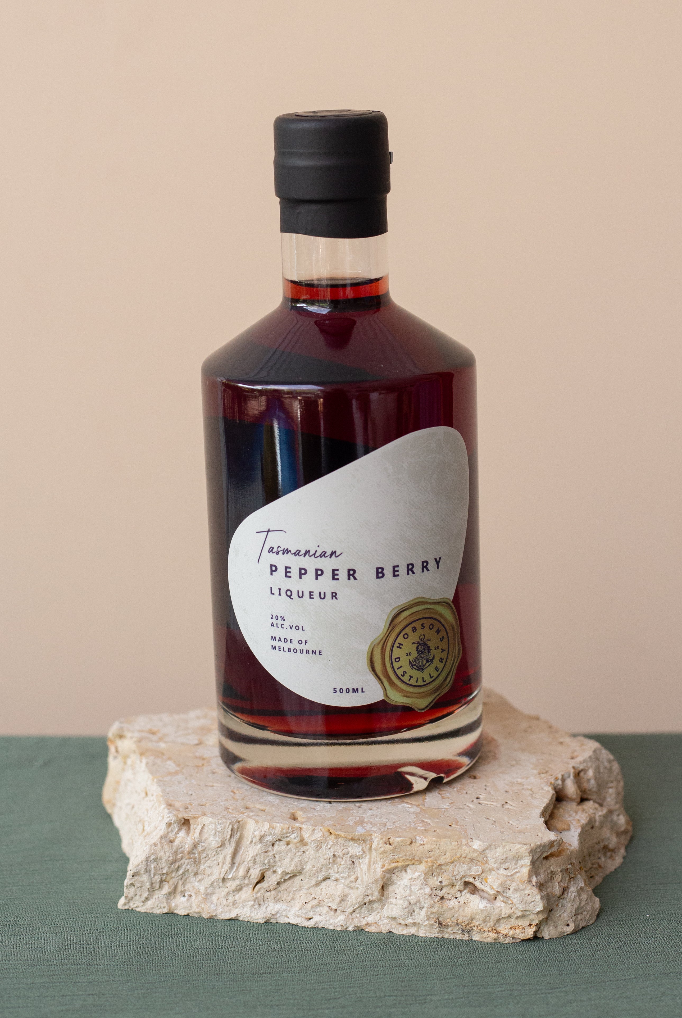 Bottle of Tasmanian Pepper Berry Liqueur on a stone surface with a beige background