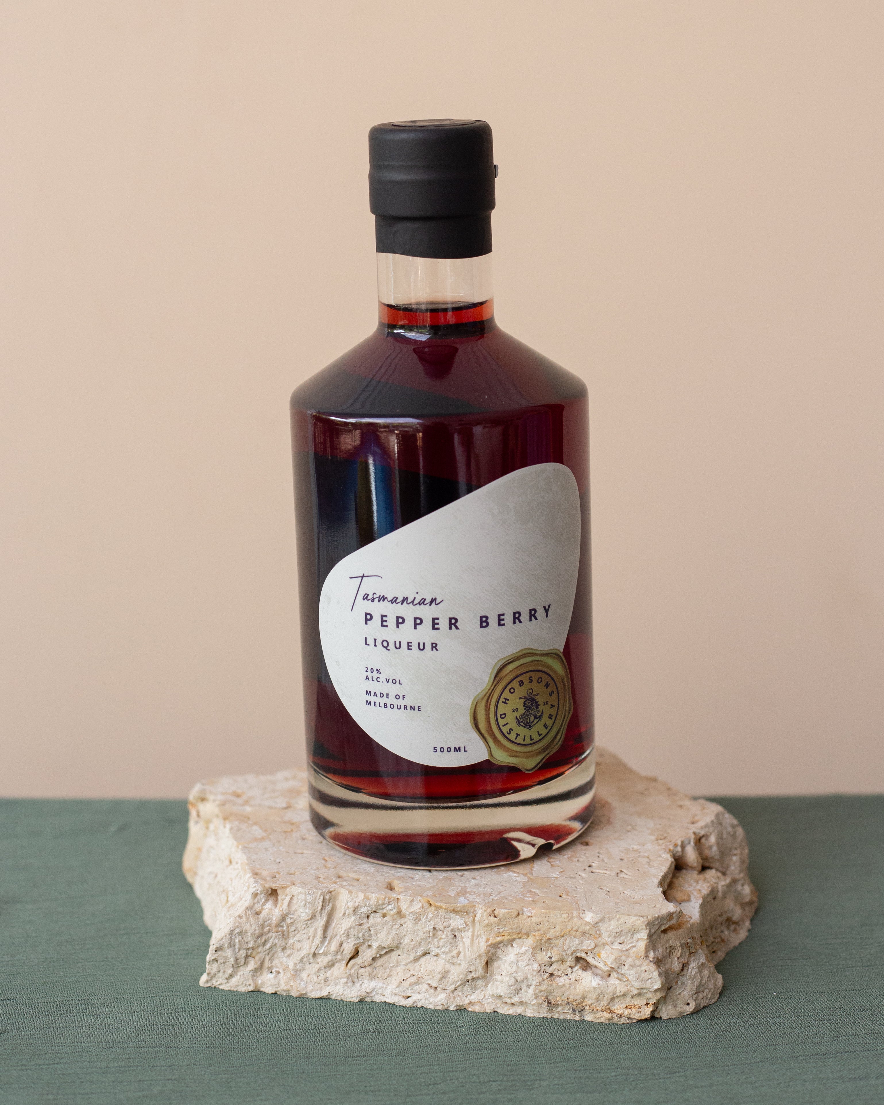 Bottle of Tasmanian Pepper Berry Liqueur on a stone surface with a beige background